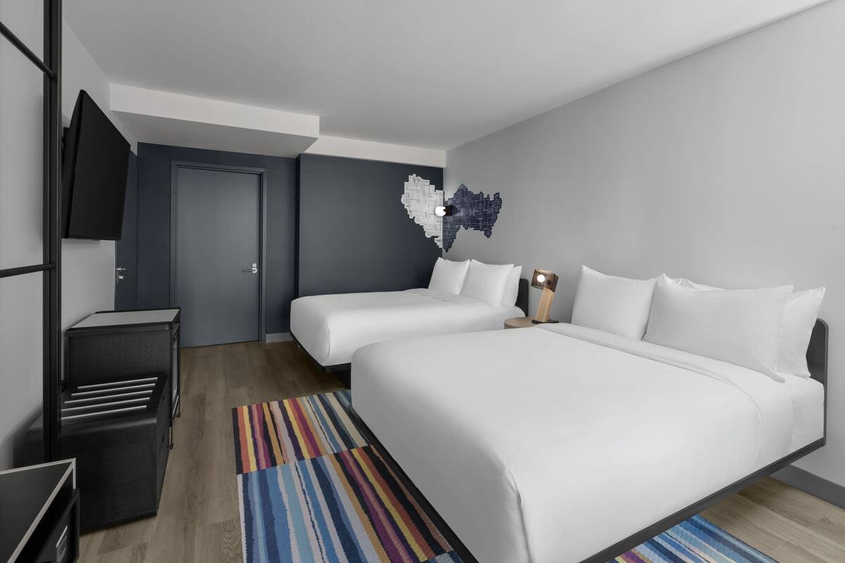 A modern hotel room with two beds, a TV, and a unique wall art piece.