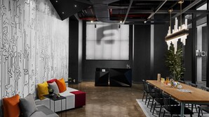 A modern conference room with a large screen, a sofa with colorful cushions, a wooden table, and black chairs. - Aloft by Marriott New York Chelsea (New York)
