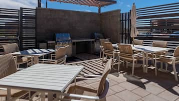 Eine Terrasse im Freien mit Tischen, Stühlen, einem Grill und einer Pergola.
