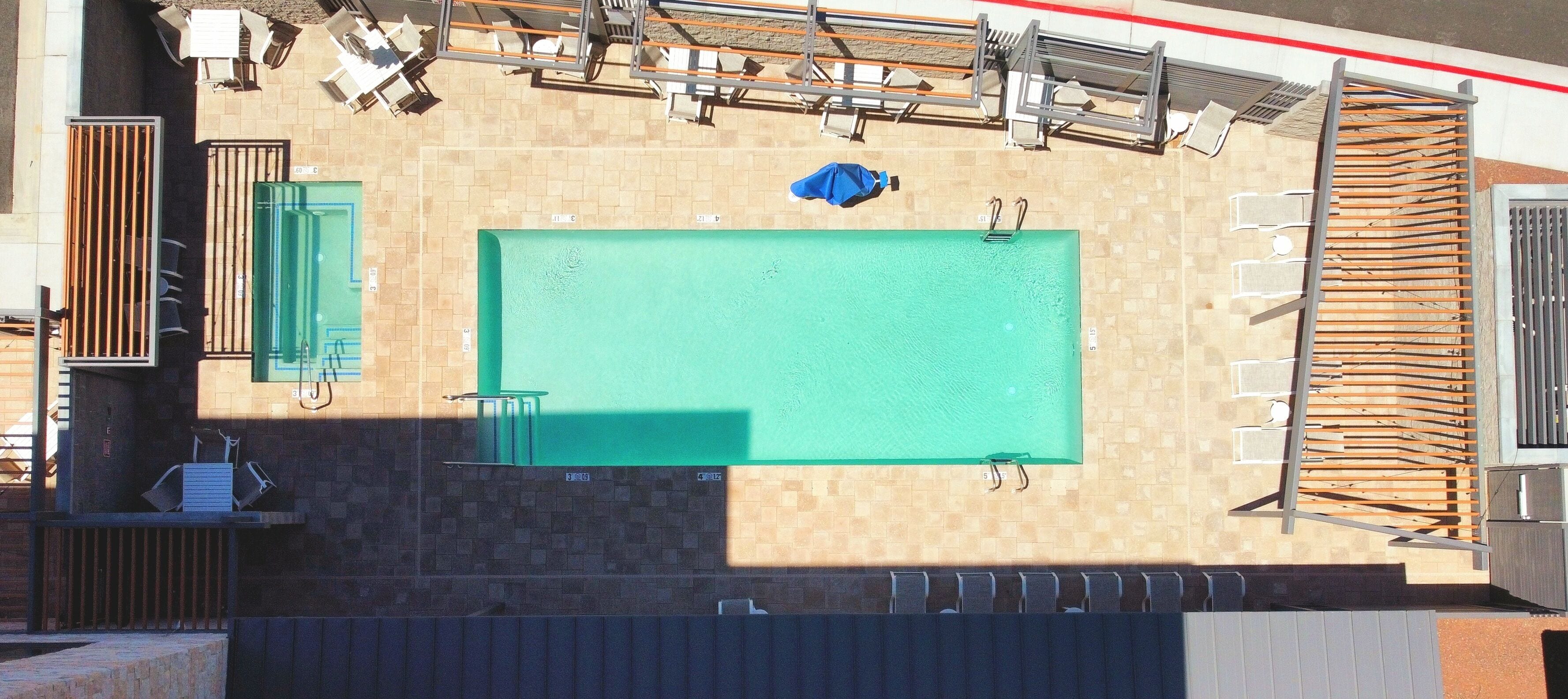 A rooftop pool area with a rectangular pool, sun loungers, and a covered seating area.