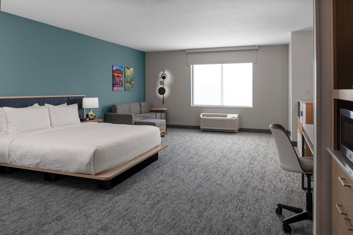 A hotel room with a bed, a desk, a chair, a TV, a window, and a wall with a poster.