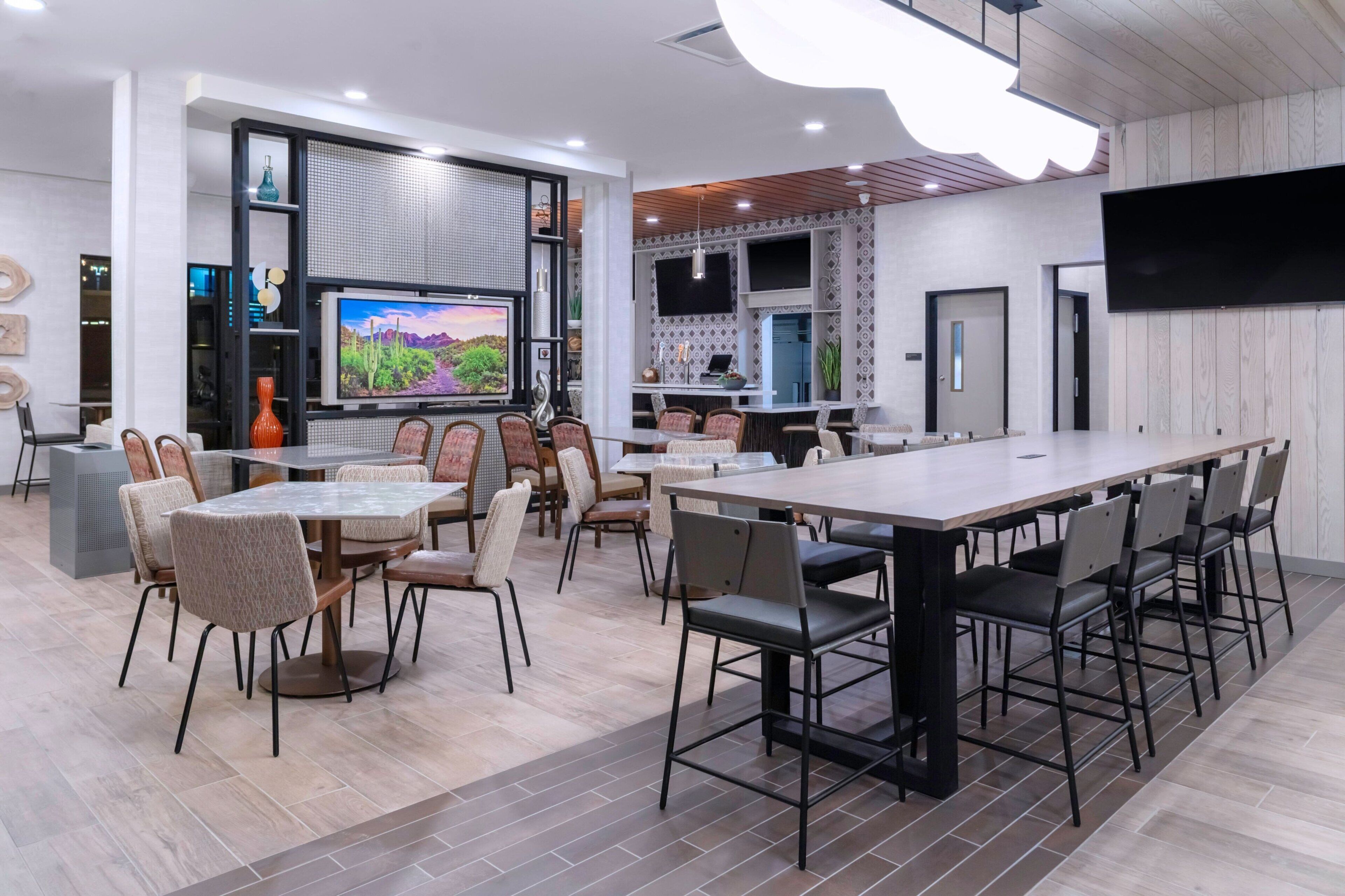 Un comedor moderno con una mesa grande y sillas, un televisor montado en la pared y una zona de cocina con una pantalla grande.
