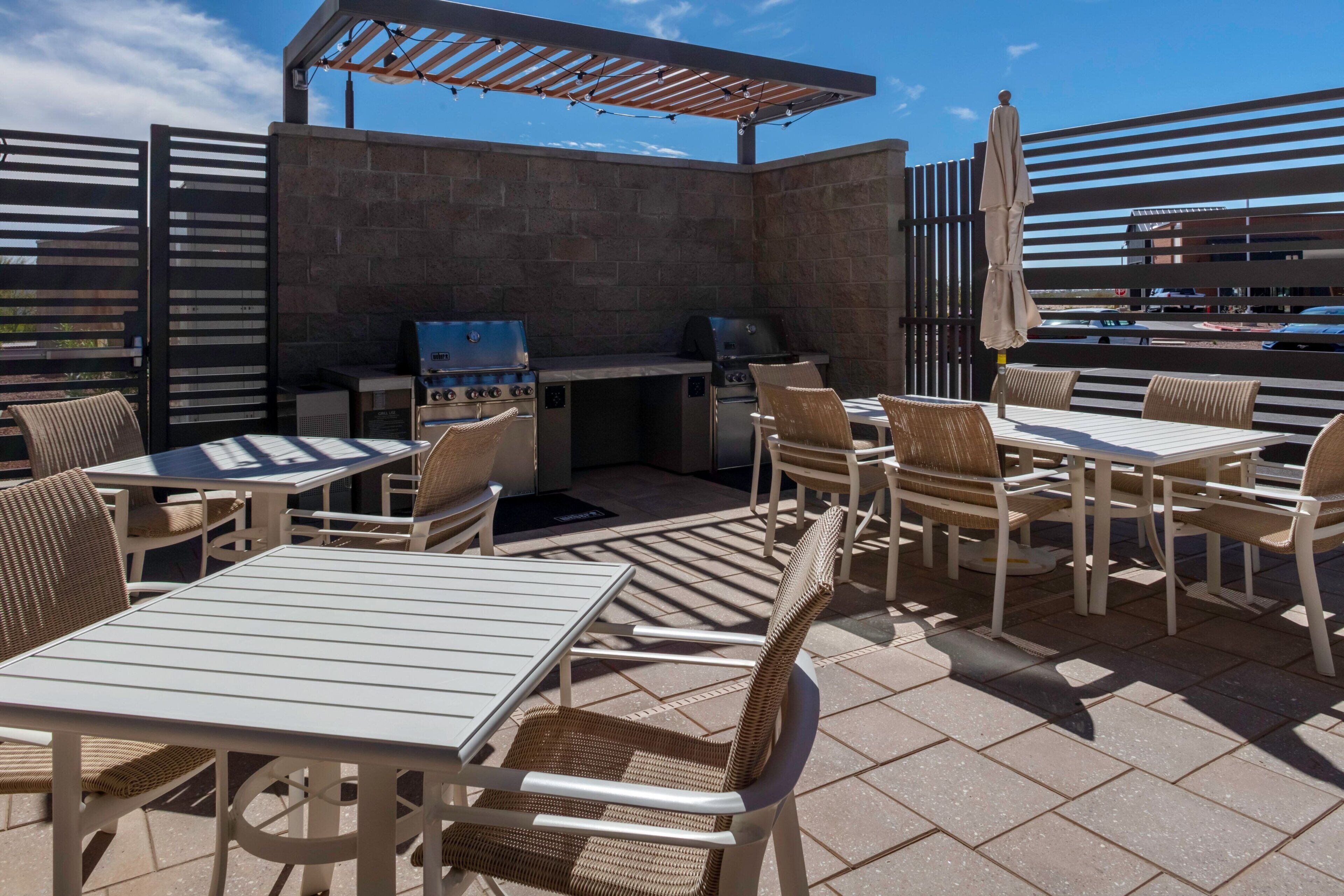 An outdoor patio area with tables and chairs, a grill station, and a pergola providing shade.