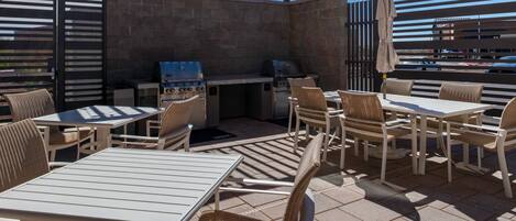 An outdoor patio area with tables and chairs, a grill station, and a pergola providing shade.