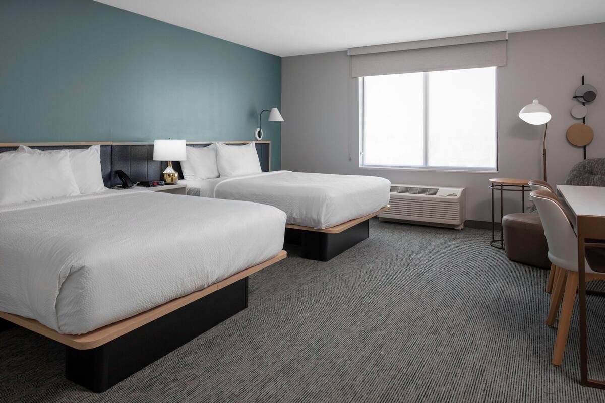 A hotel room with two beds, a desk, a chair, a lamp, a phone, and a window.