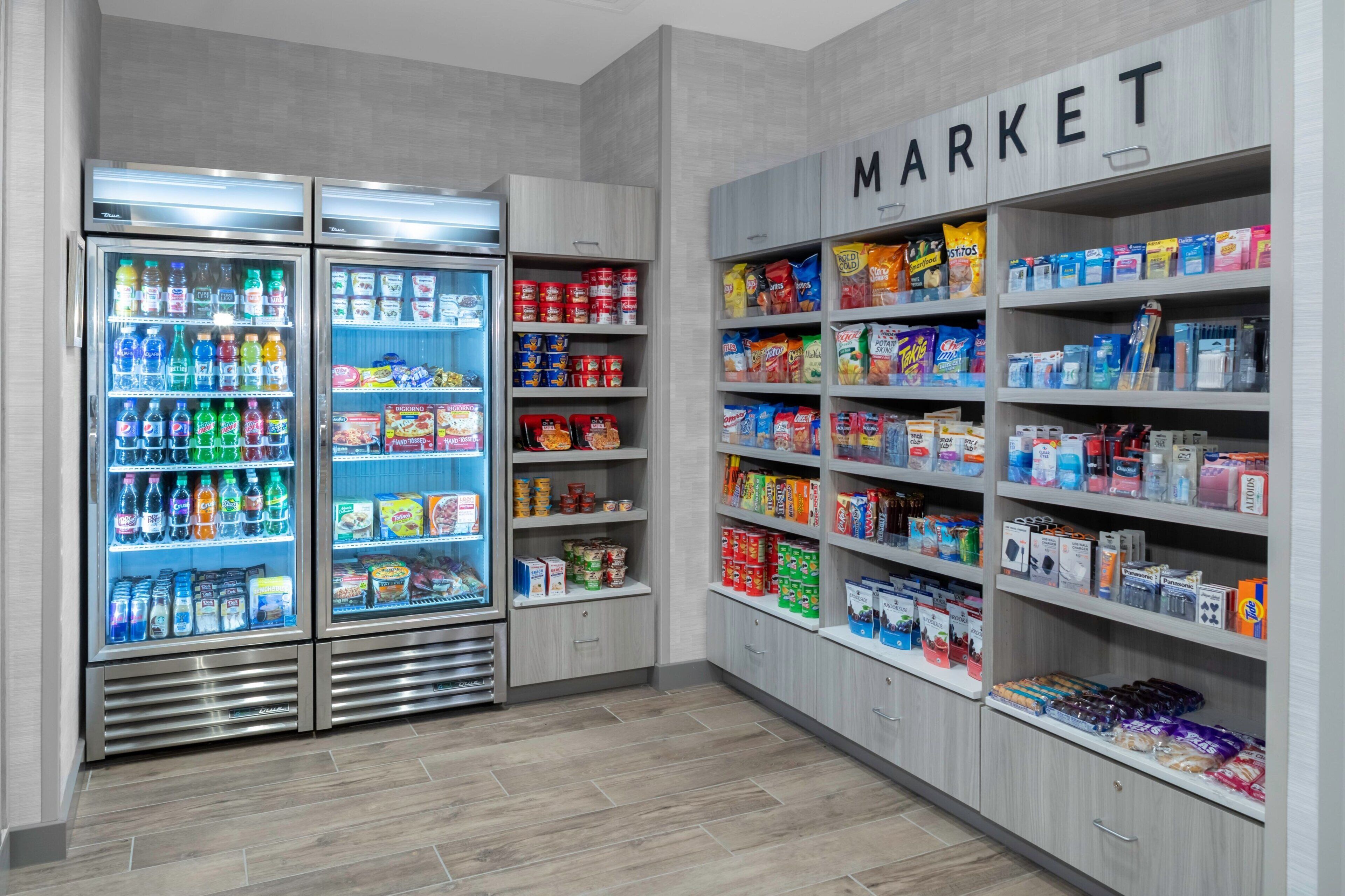 A grocery store with refrigerated beverage coolers, shelves stocked with snacks, and a 'MARKET' sign.