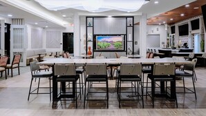 A spacious dining area with a long table and multiple chairs, a television screen, and a kitchen area with wooden cabinets and modern appliances. - TownePlace by Marriott Suites Buckeye Verrado (Buckeye)