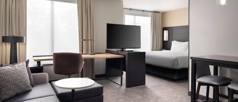 Une chambre d’hôtel comprenant un canapé, un bureau avec un téléviseur à écran plat, un lit et une petite table avec deux tabourets.
