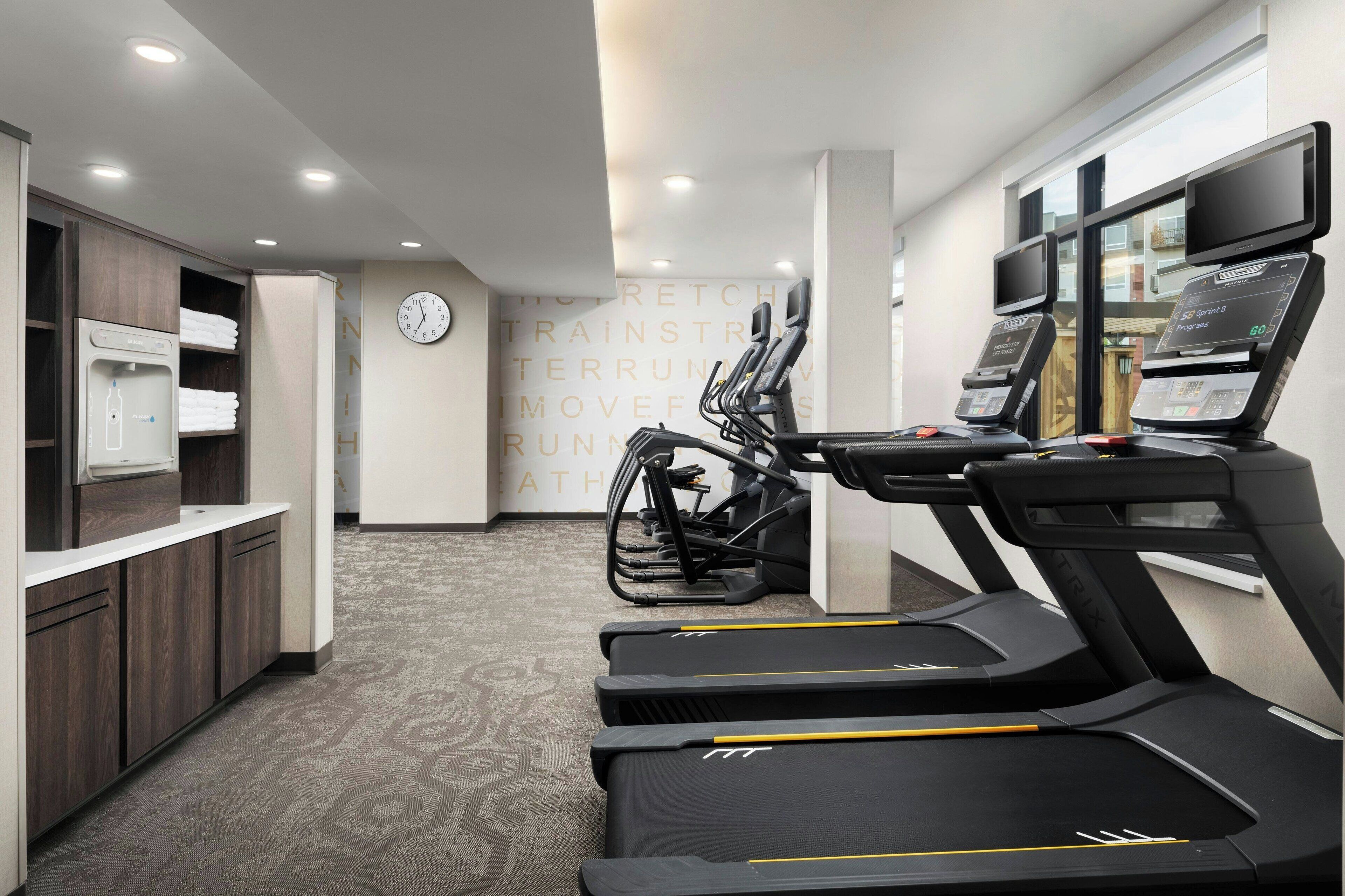 Ett modernt gym med löpband, en motionscykel och en väggklocka.