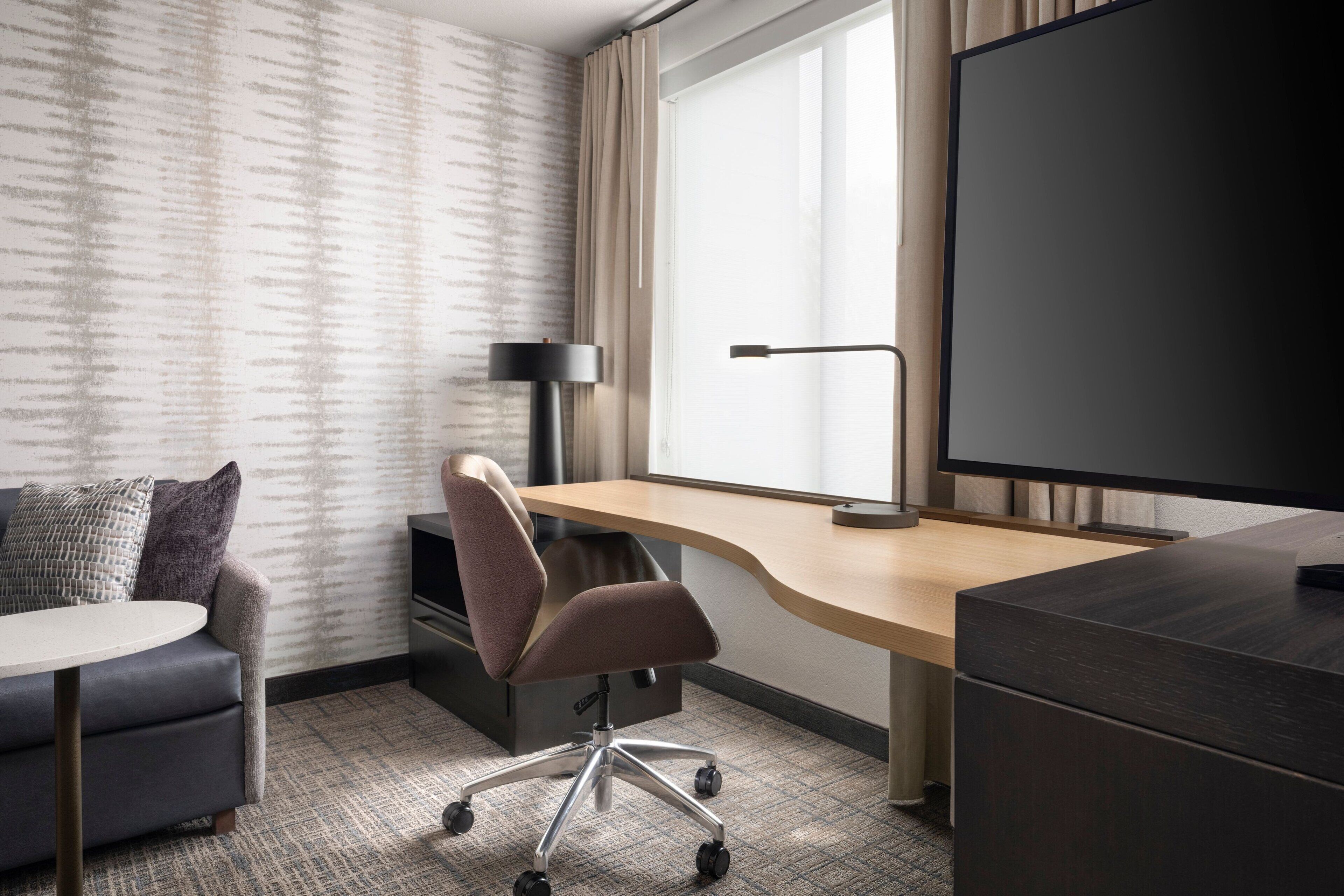 Een hotelkamer met een bureau, stoel, televisie en een bank.