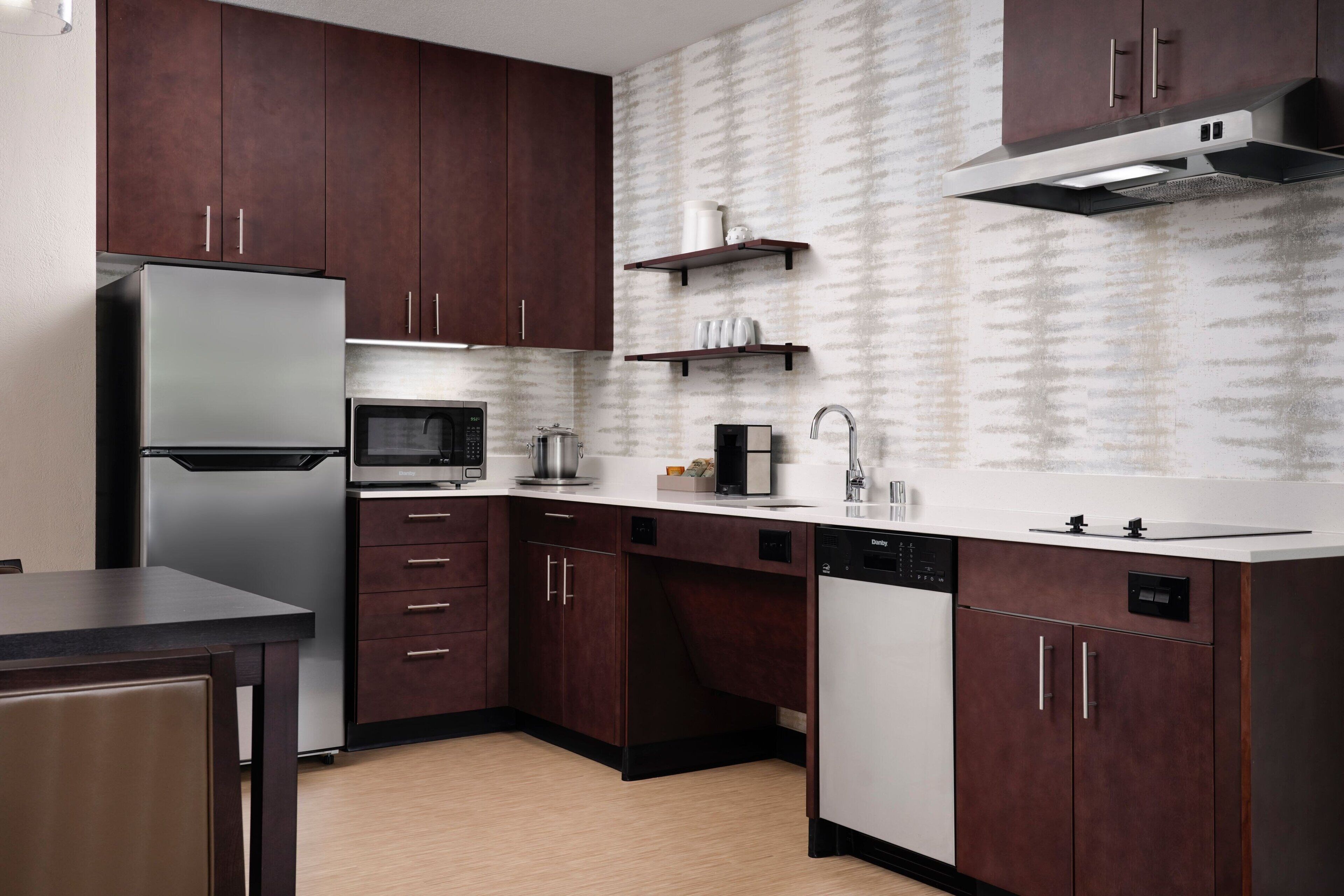 A modern kitchen with dark wooden cabinets, stainless steel appliances, and a patterned backsplash.