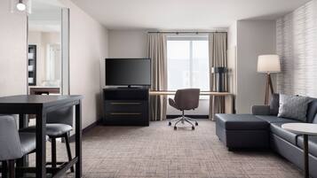 A modern hotel room with a desk, chair, sofa, and a TV.