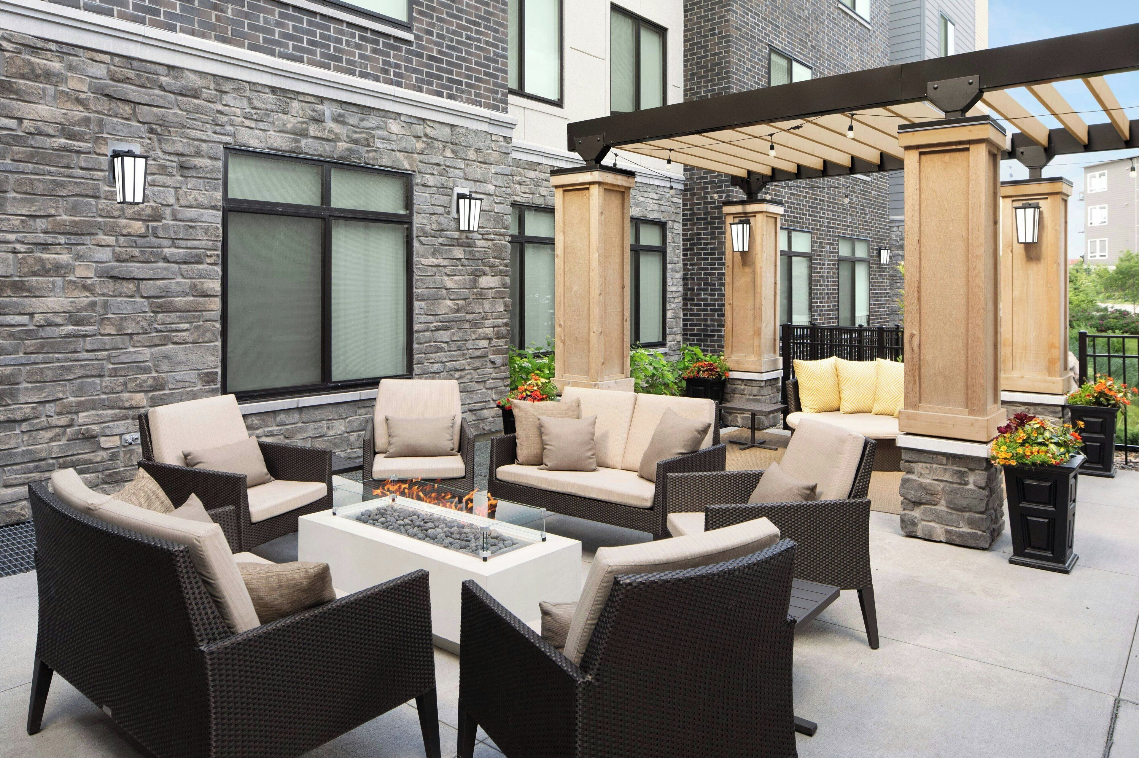 An outdoor patio with wicker furniture, a stone wall, and a pergola.