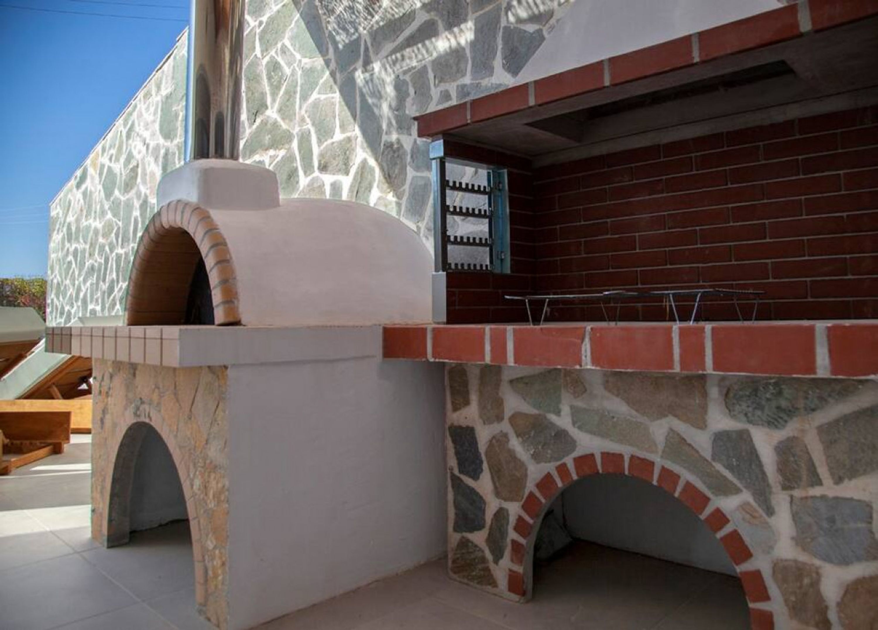 Een buitenkeuken met een ontwerp van steen en baksteen, inclusief een ingebouwde oven en een aanrecht met een grill.