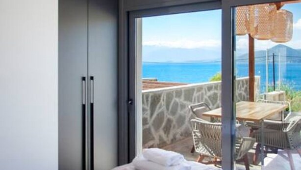 A bedroom with a bed, a large window, and a view of the sea. - Villa Petalouda Paleros (Aktio-Vonitsa)