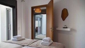A hotel room with two beds, a wooden door, a mirror, a small stool, and a shelf with toiletries. - Villa Petalouda Paleros (Aktio-Vonitsa)