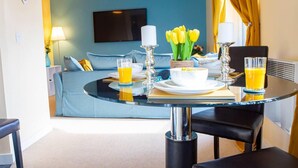 A modern hotel room with a dining area featuring a round table, chairs, and a breakfast setup including a bowl, plates, and glasses of orange juice. - Inviting 2-bed Apartment in Wolverhampton (Wolverhampton)