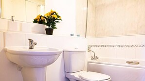 A bathroom with a white sink, toilet, and bathtub. There is a mirror above the sink and a potted plant with yellow flowers on the counter. - Inviting 2-bed Apartment in Wolverhampton (Wolverhampton)