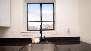 A kitchen with a stainless steel sink, a window with a view of buildings, and a white wall. - Honeymoon in Hotsprings (Hot Springs)