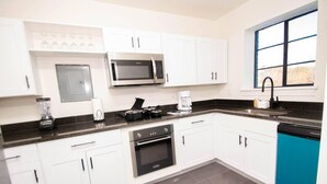 A modern kitchen with white cabinets, a black countertop, a microwave, a coffee maker, and a dishwasher. - Honeymoon in Hotsprings (Hot Springs)
