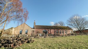 Un bâtiment en pierre avec un toit recouvert de tuiles rouges, une cheminée et une clôture en bois.