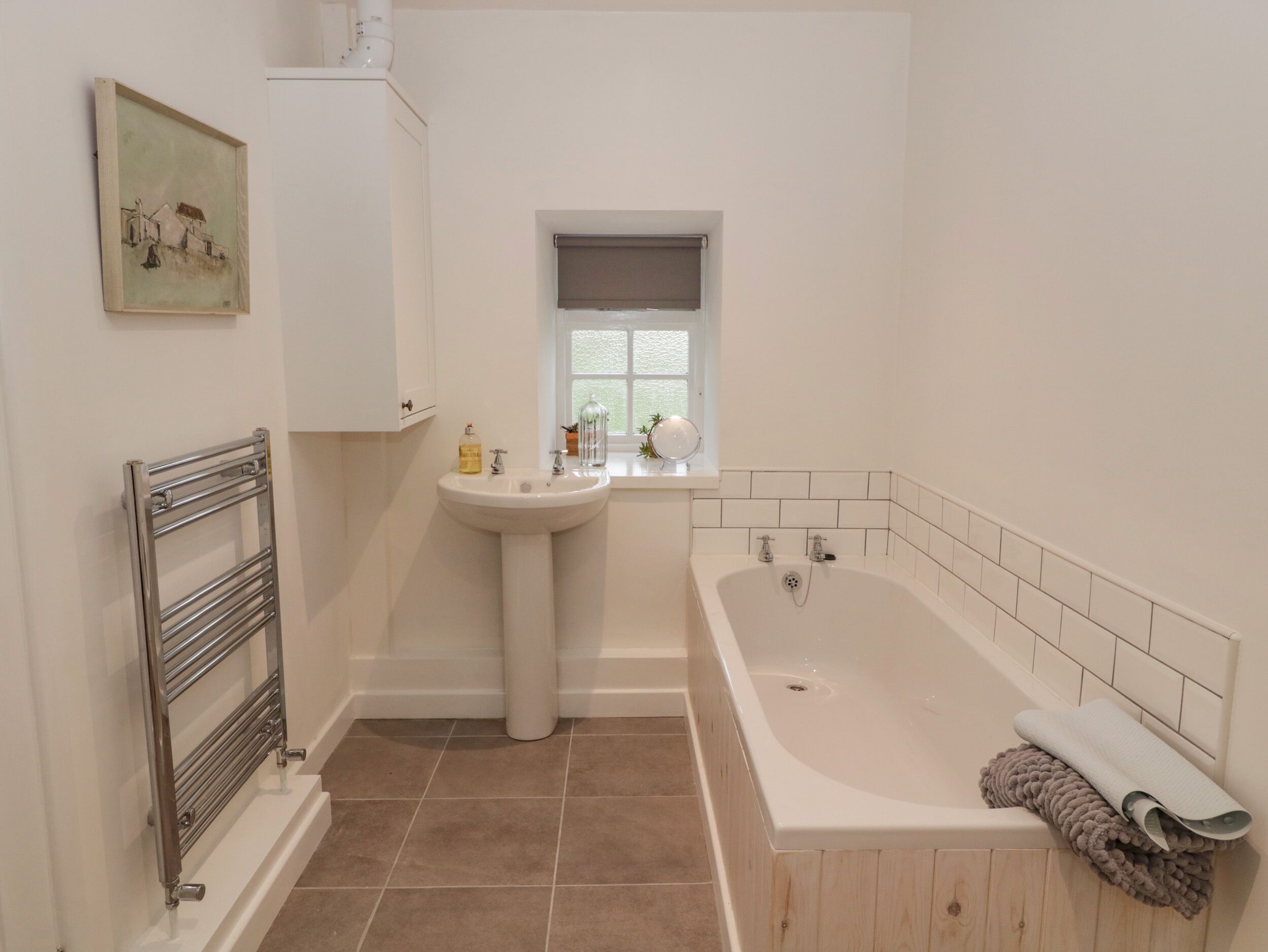 Un baño con bañera, lavamanos, toallero y ventana.