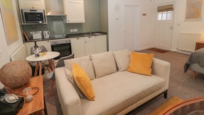 Un espacio habitable compacto con kitchenette, un sofá con cojines amarillos, una pequeña mesa de comedor y un teléfono antiguo.