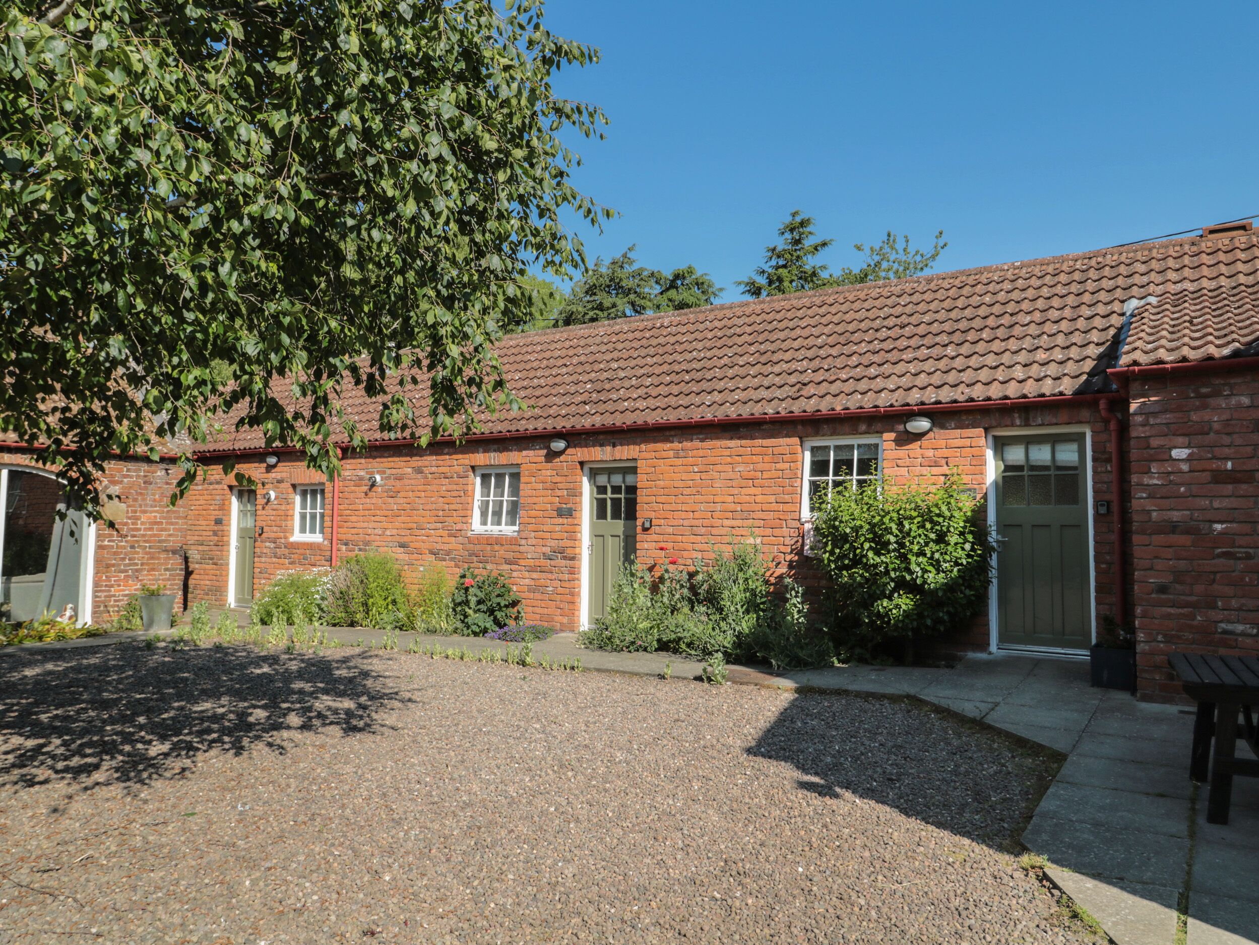 A brick building with a tiled roof, a gravel driveway, and a garden with various plants.