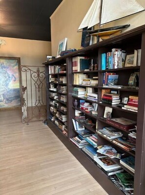 Una biblioteca con estanterías llenas de libros, una puerta metálica decorativa y un cuadro en la pared.
