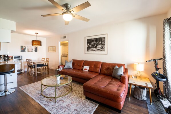 A modern living room with a leather sofa, a glass coffee table, a dining area with a table and chairs, and a kitchen area with a bar stool. - ASU Tempe Modern Condo (Tempe)