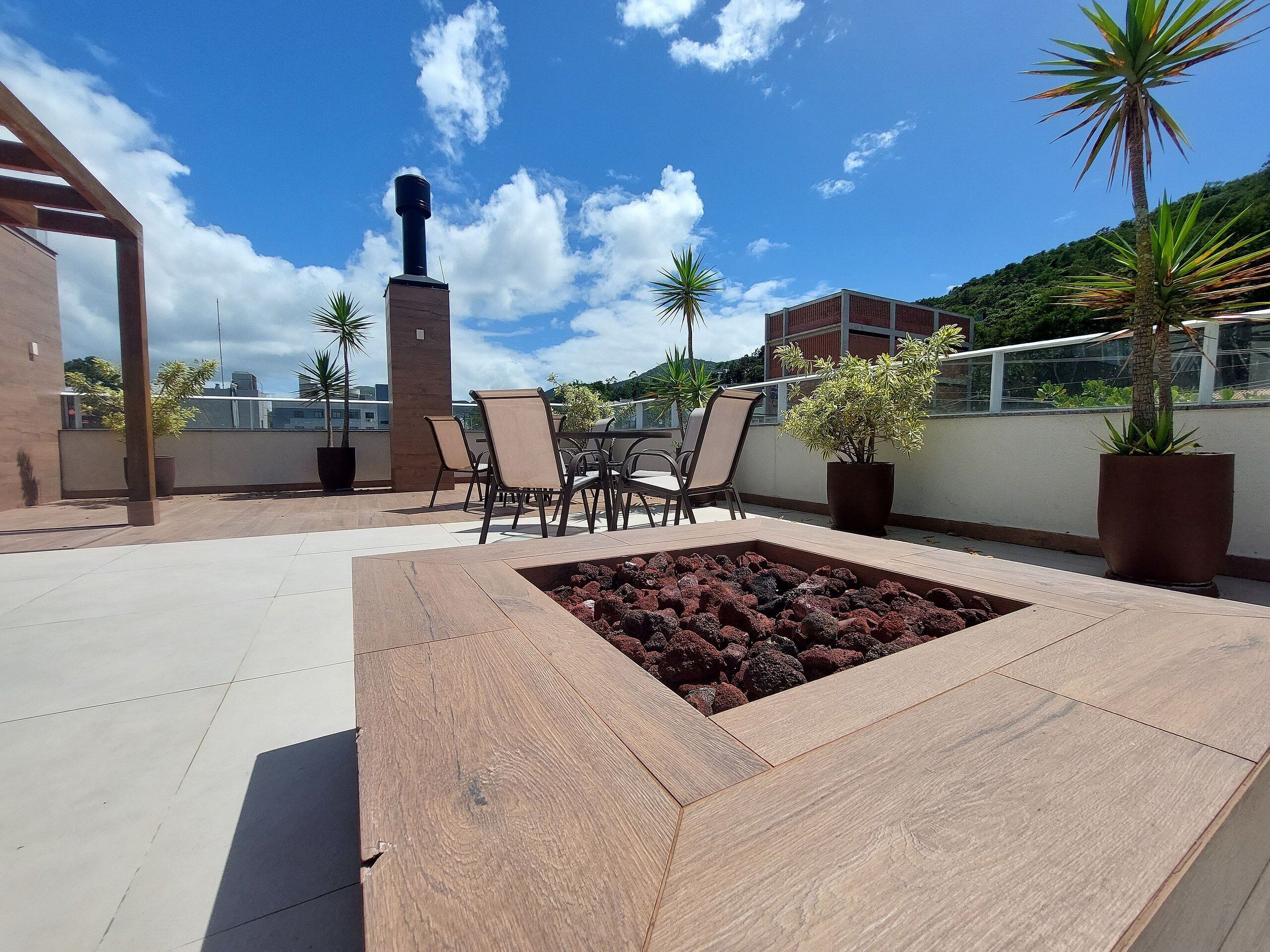 A rooftop terrace with a fire pit, seating area, and potted plants.
