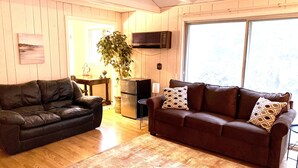 A living room with two sofas, a wooden floor, a plant, a TV, and a window. - Spacious House short walk to Bills Stadium (Orchard Park)