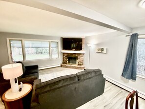 Un salon avec une cheminée, un canapé, une lampe et une grande fenêtre.
