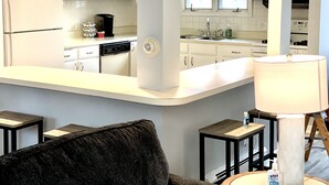 A modern kitchen with white cabinets, a dishwasher, and a coffee maker. There is a large mirror reflecting the kitchen, and a lamp on a side table. - Spacious House short walk to Bills Stadium (Orchard Park)