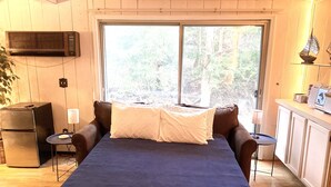 A bedroom with a large bed, a television mounted on the wall, a small table with a lamp, and a view of the outdoors through a large window. - Spacious House short walk to Bills Stadium (Orchard Park)