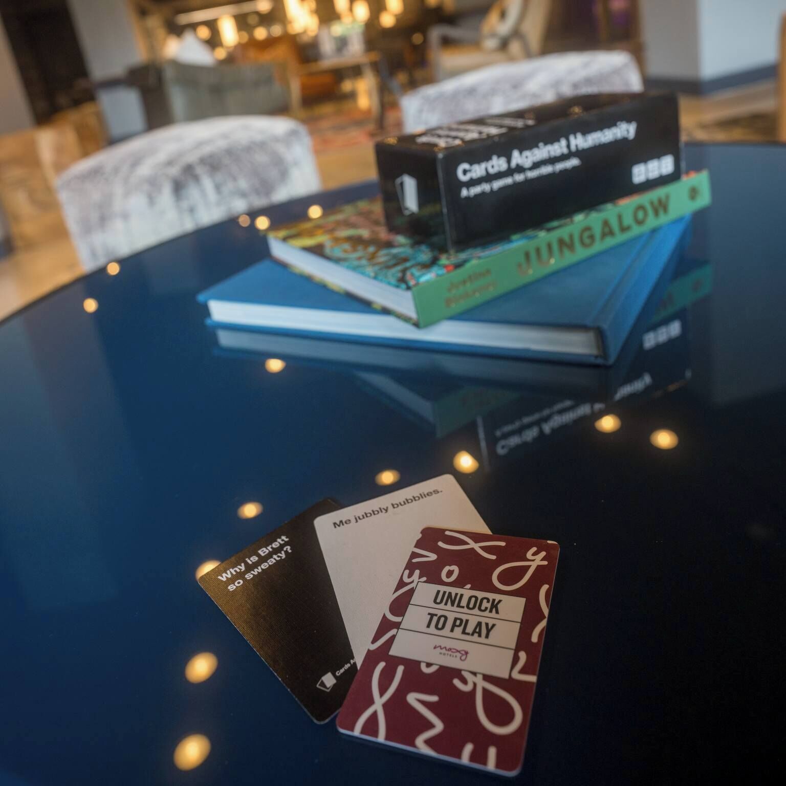 Une table sur laquelle se trouve une boîte de jeu de cartes portant l’inscription « Cards Against Humanity » et un livre intitulé « JUNGALOW ».