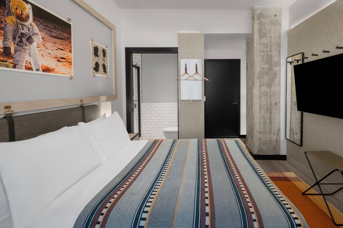 Quarto de hotel com uma cama grande, televisão de tela plana, guarda-roupa e casa de banho visível através de uma porta aberta.