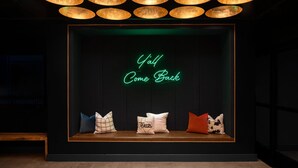 A dark room with a neon sign reading "Y'all Come Back" and a bench with pillows. - Moxy Houston Downtown (Houston)
