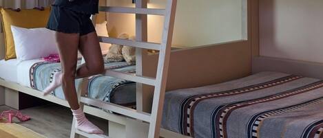 A bunk bed room with a ladder, a bed with patterned bedding, and a suitcase on the bed.