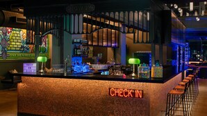 A bar area with a neon 'CHECK IN' sign, a bar counter, and a seating area with stools. - Moxy Houston Downtown (Houston)