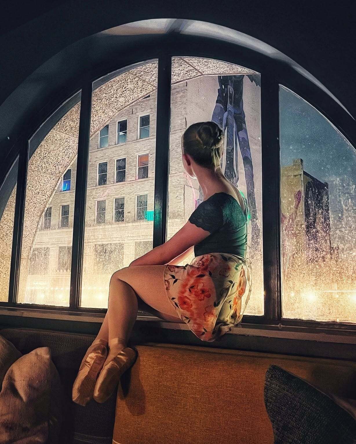A person sitting by a window with a view of a building.