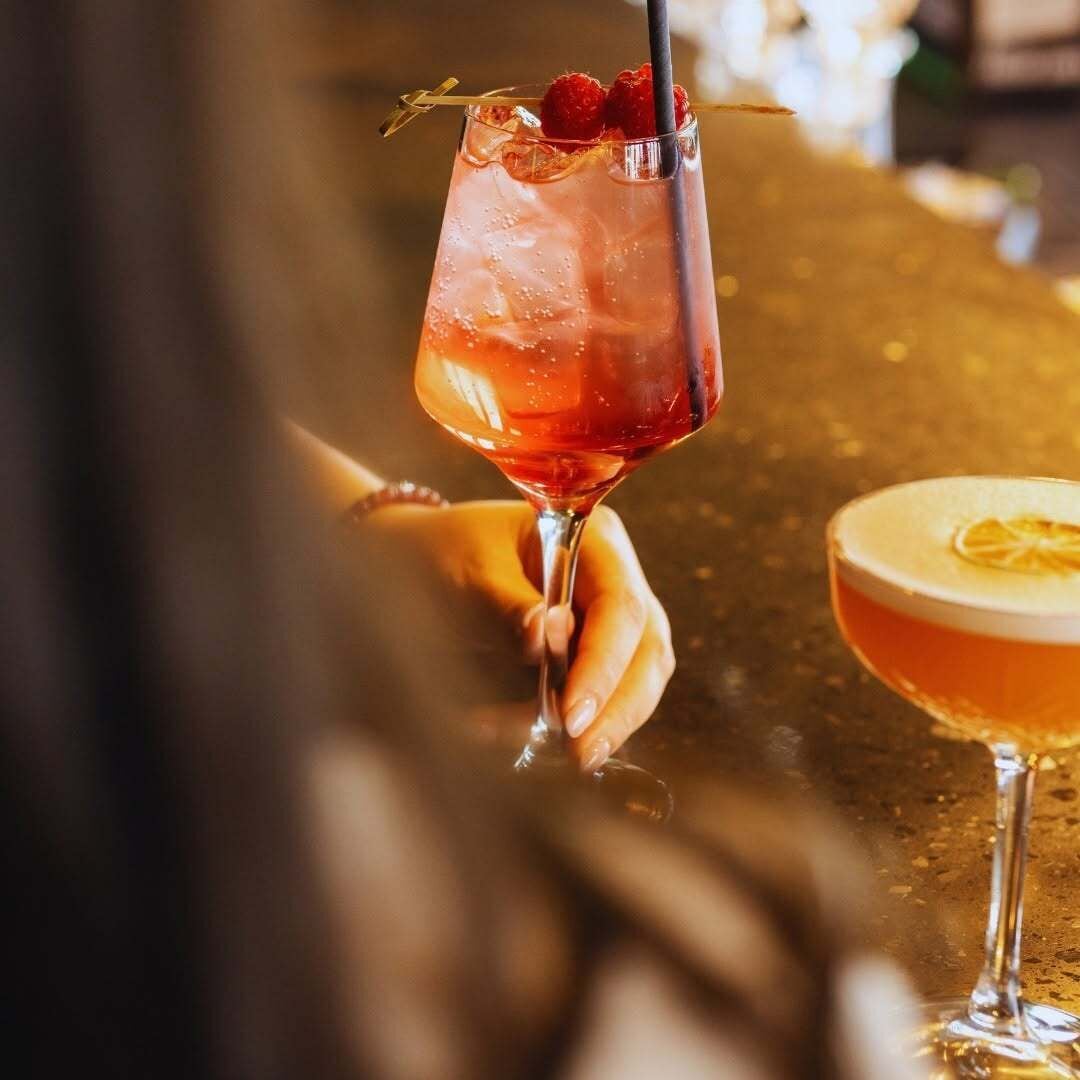 A cocktail glass with ice cubes and a straw, garnished with a raspberry and a lemon slice.
