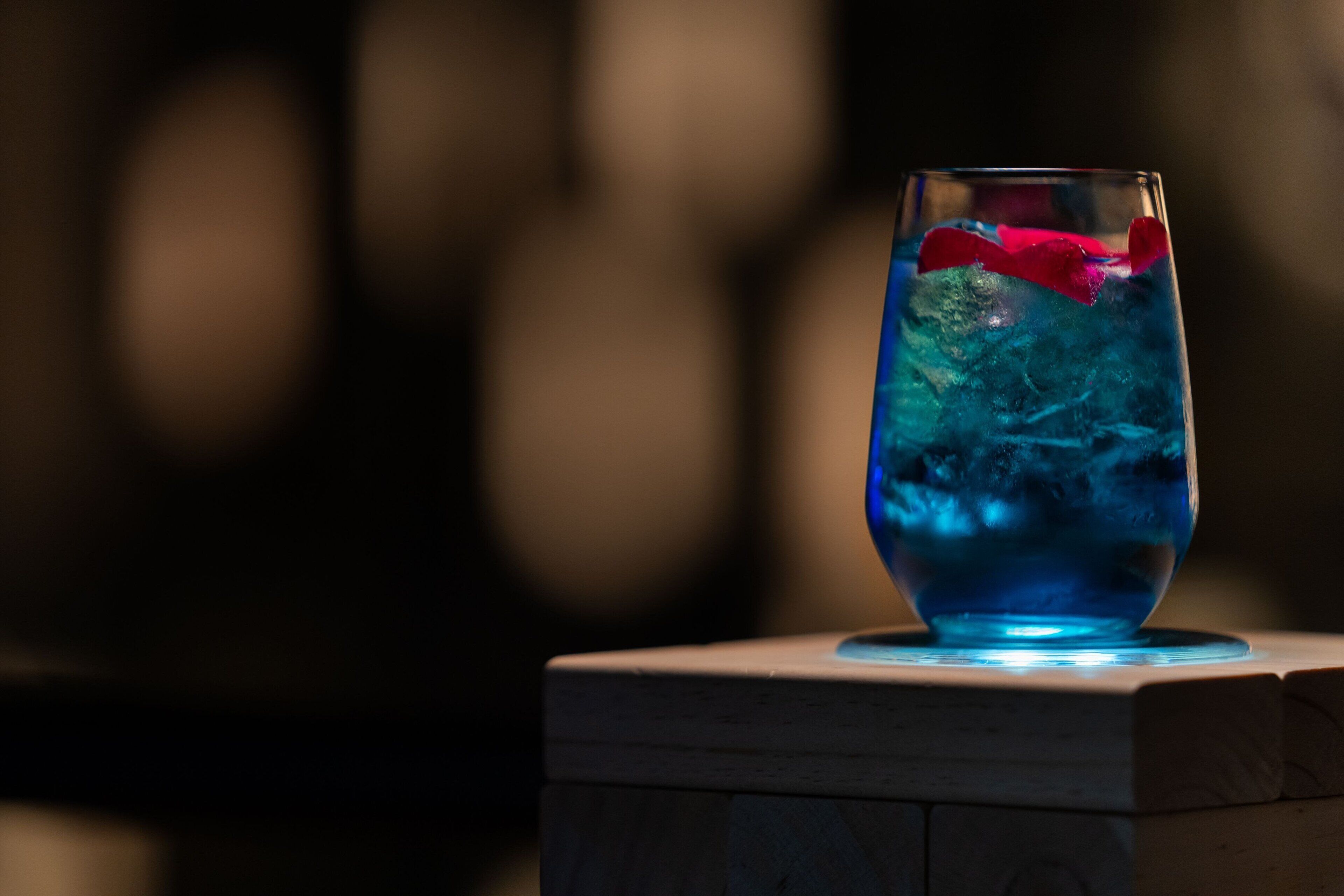 Um copo com líquido azul e um objeto vermelho sobre uma superfície de madeira.