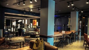 A modern lounge area with leather seating, a wooden table, and a bar area. - Moxy Houston Downtown (Houston)