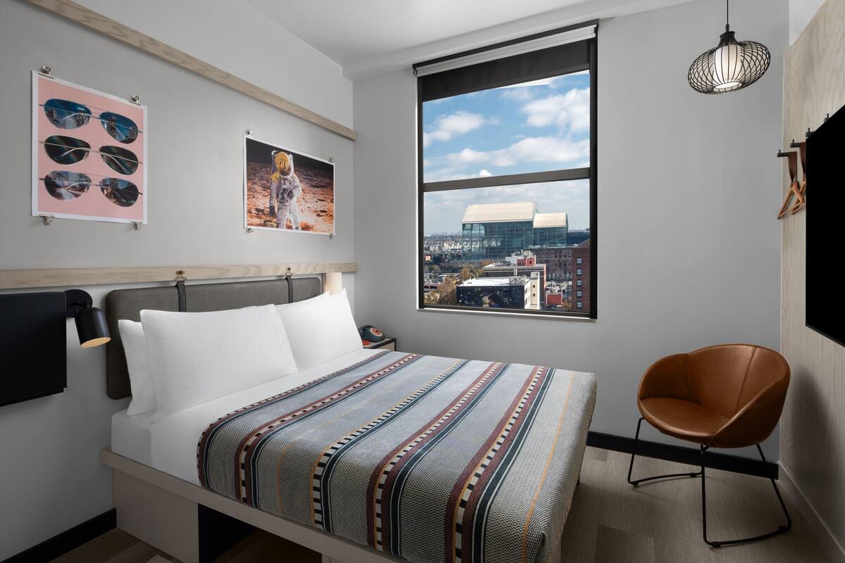 Quarto de hotel moderno com uma cama grande, vista da cidade e obras de arte na parede.