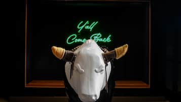 A bull statue with a neon sign in the background that reads "Y'all Come Back".