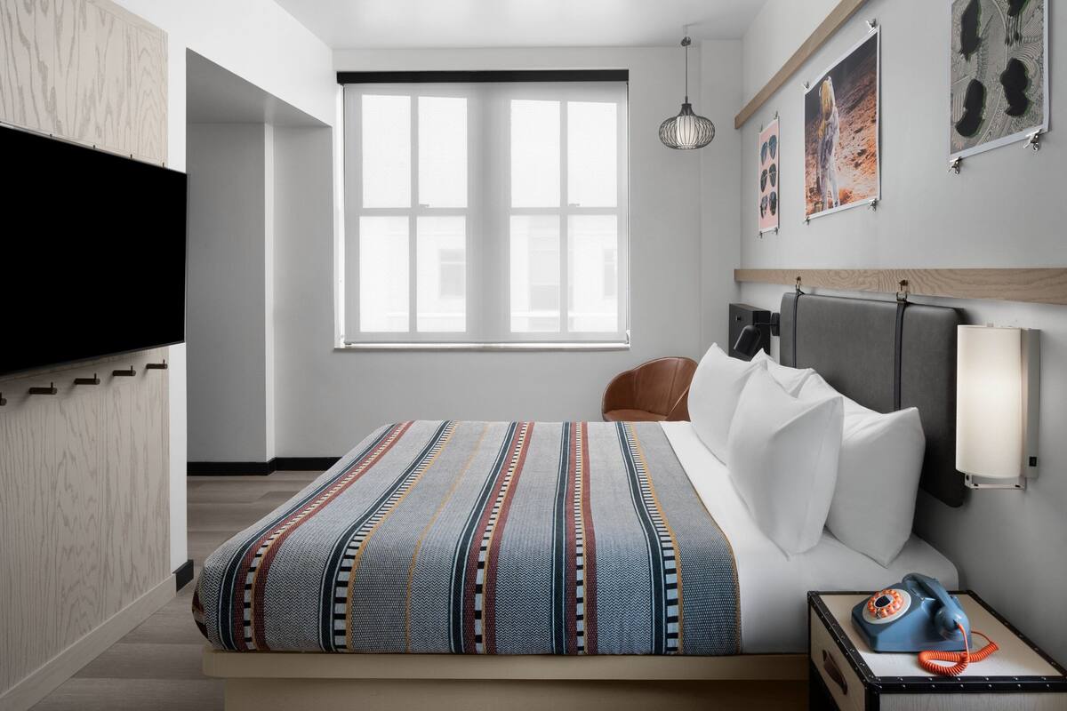 Quarto de hotel moderno com uma cama grande, mesa de cabeceira com telefone, televisão na parede e obras de arte.
