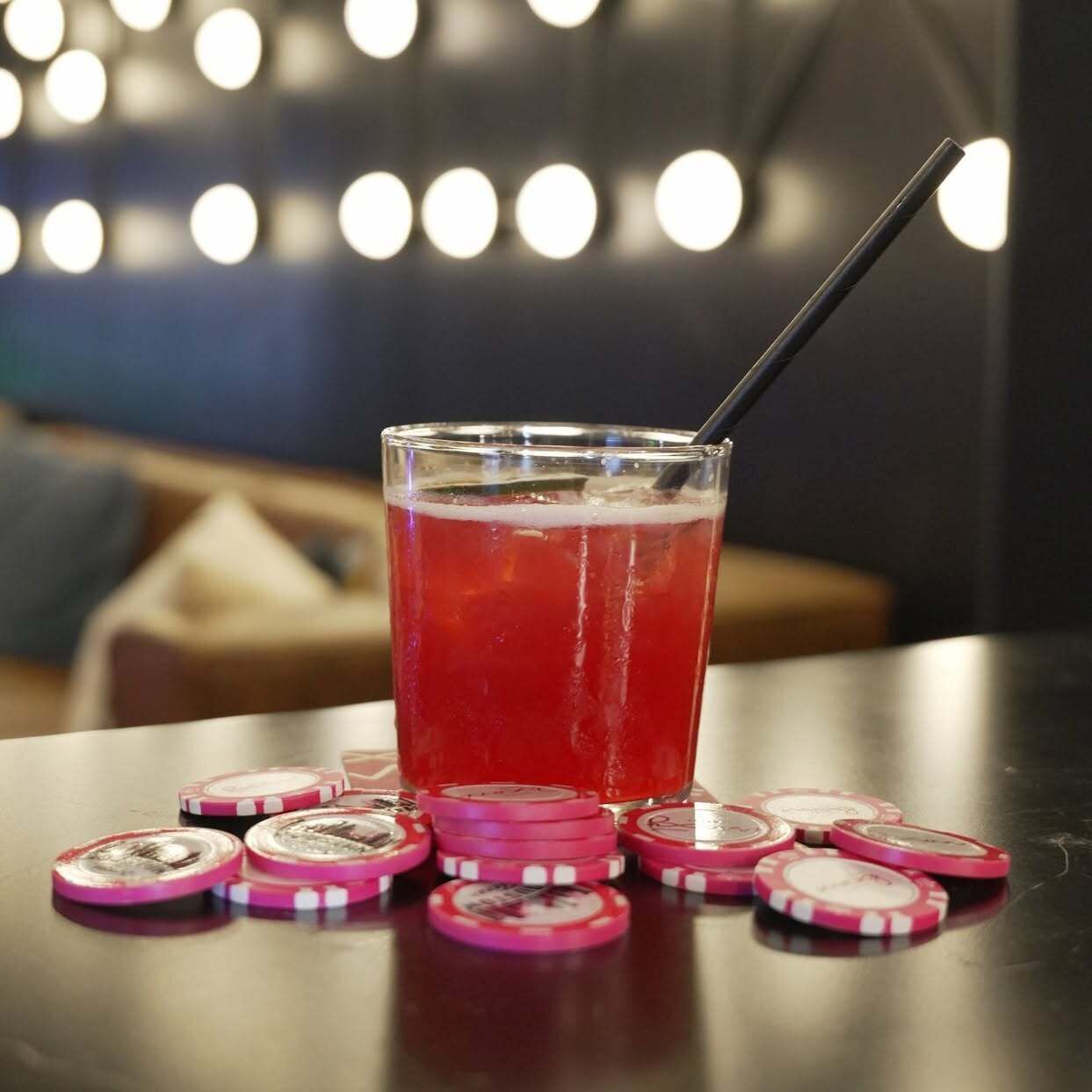 Ein Glas rotes Getränk mit Trinkhalm auf einer Tischplatte, umgeben von Pokerchips.