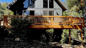Een chalet met twee verdiepingen, een houten terras en grote ramen.