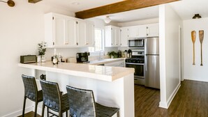 Een moderne keuken met witte kasten, een centraal eiland met barstoelen, een roestvrijstalen koelkast en houten balken in het plafond.